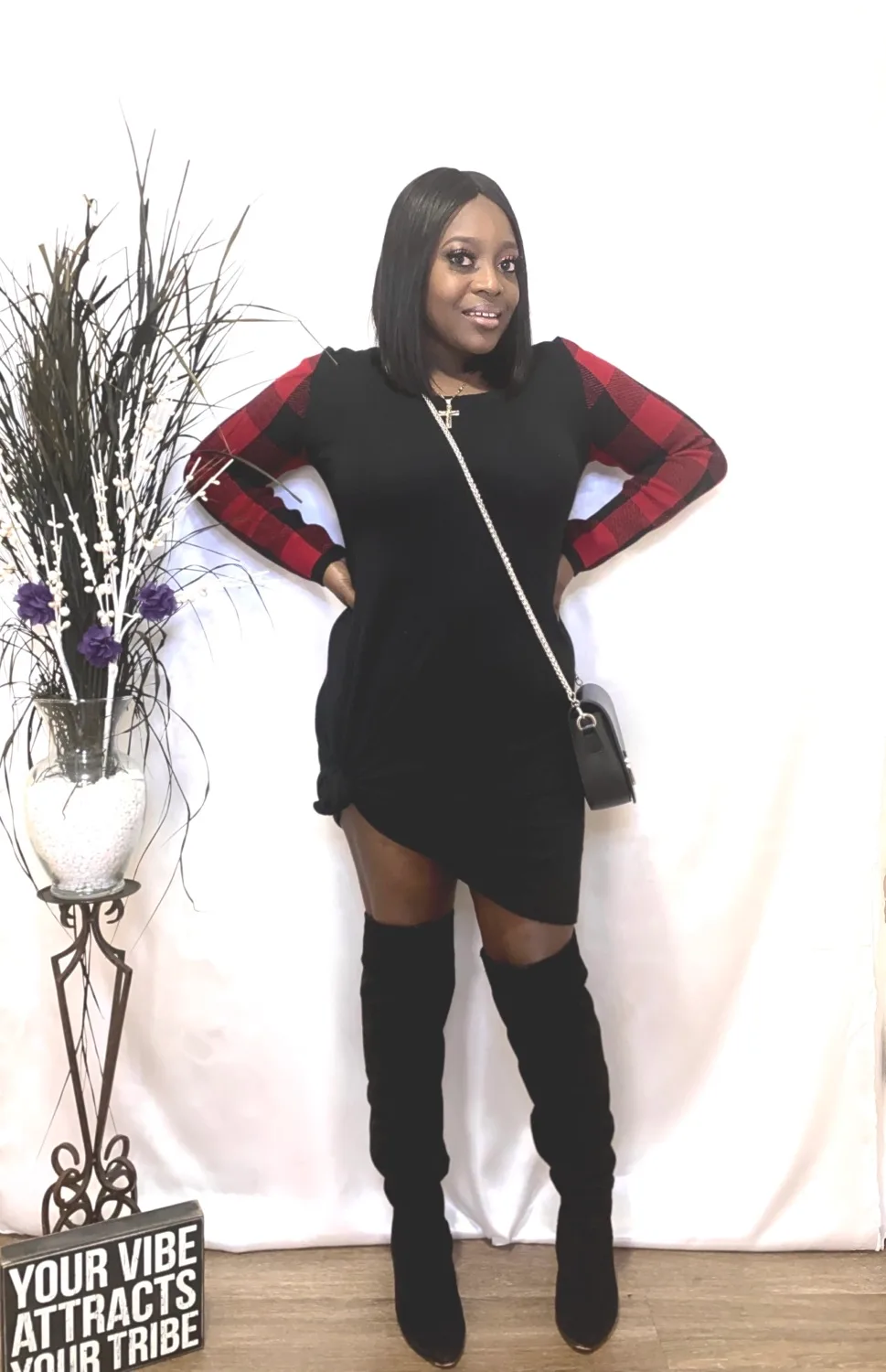 Smiling woman in black mini dress with red sleeves, thigh-high boots
