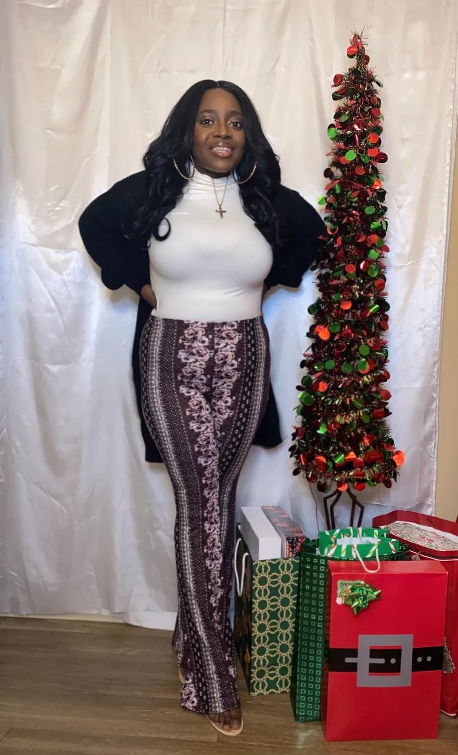Smiling woman in sparkly pants by Christmas tree and gifts.