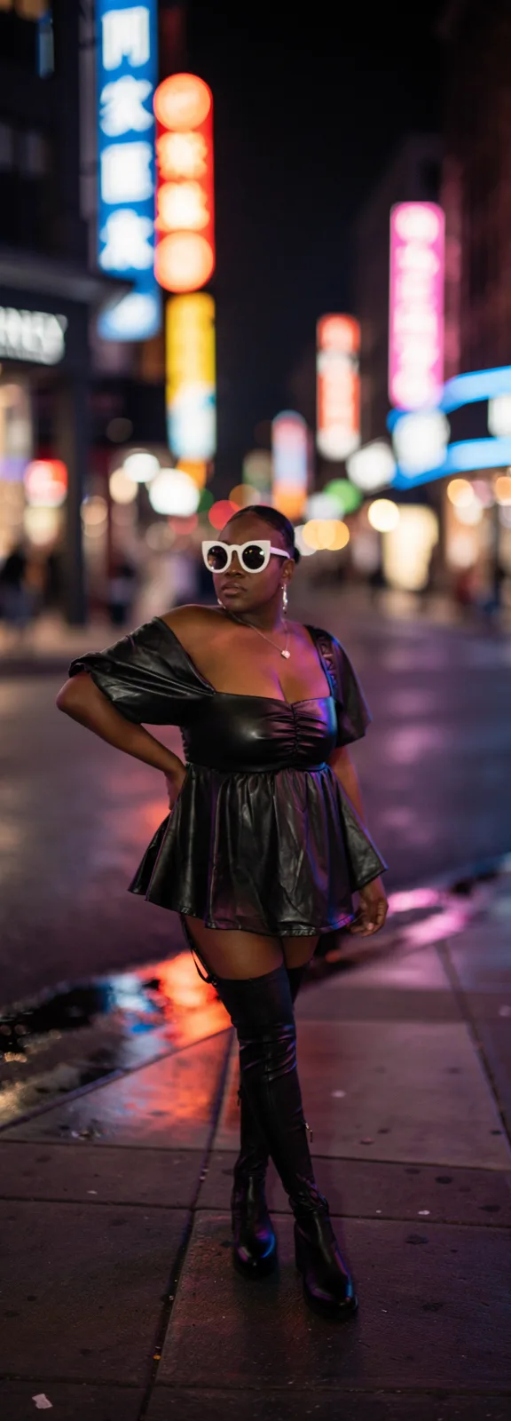 Woman in black peplum outfit and boots in city at night
